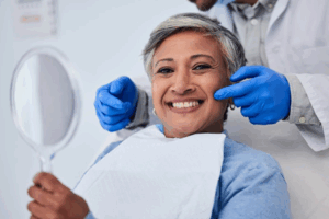 Dentist pointing to a patient’s smile as she grins while holding a mirror